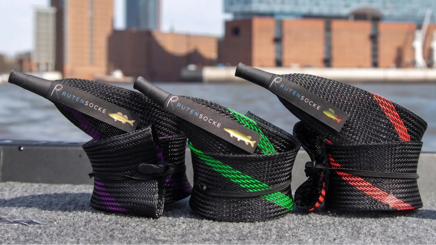 Drei schwarze geflochtene Halter für Angelnetz-Seil, jeweils mit einem unterschiedlich gefärbten Streifen, lila, grün und rot, und mit dem Branding „rutensocke“ sowie einem Fisch-Logo versehen.