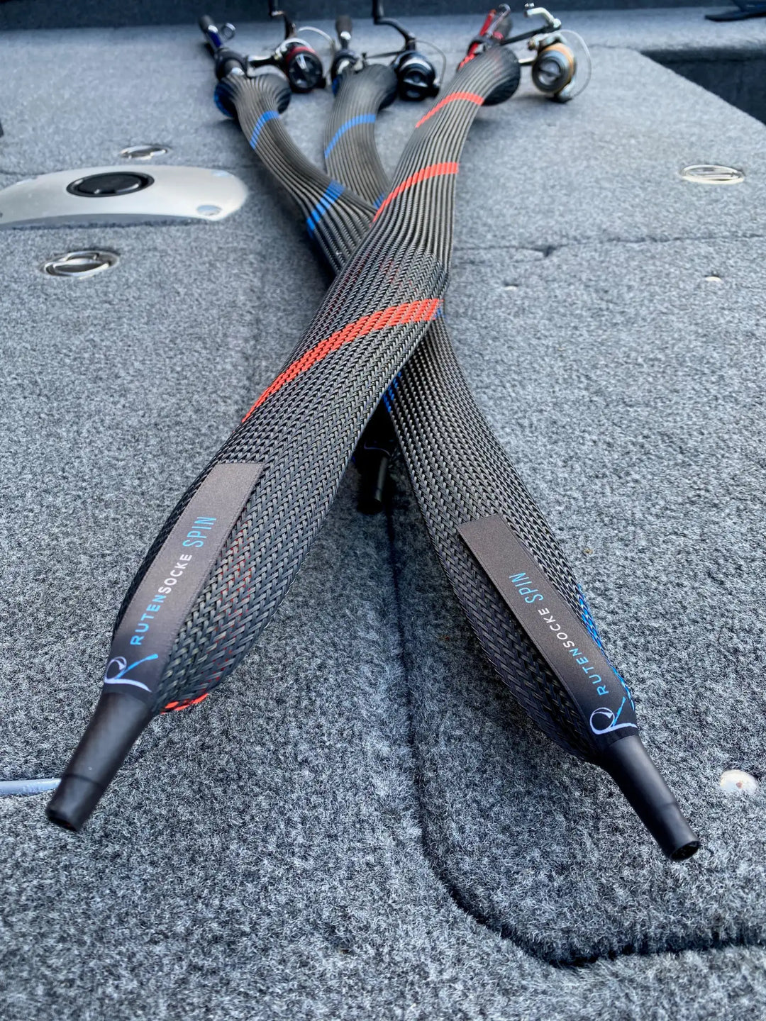 Schwarze gewebte Angelrutenhüllen mit roten und blauen Akzentstreifen, mit der Marke 'rutendo spinn' auf grauen Etiketten.