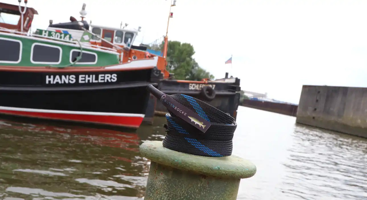 Ein schwarzer Gürtel mit blauen diagonalen Streifen und einem kleinen Fisch-Tag.